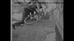 Stunt man "Zip" rides bicycle along ledge and stands on top of building News Clip