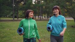 Smiling young women are walking in park with yoga mats and talking sharing news and discussing practice together. Youth, outdoor activity and conversation concept. Stock Footage