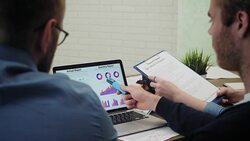 Analysts at desk work at laptop showing statistics, looking at graphs and charts Stock Footage