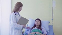 Beautiful smart Asian doctor and patient discussing and explaining something with clipboard in doctor hands while staying on Patient's bed at hospital. Medicine and health care concept. Stock Footage