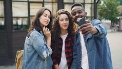 Happy male and female tourists multiethnic group are taking selfie standing in the street then watching photographs and laughing. Tourism, technology and fun concept. Stock Footage