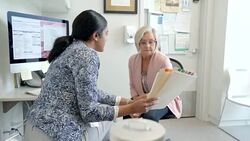 Female doctor with medical chart talking with senior woman patient in clinic doctors office Stock Footage