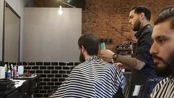 Barber trimming male customer's hair in salon Stock Footage