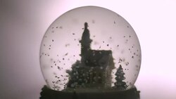 Close-up shot of 'snow' swirling round a plastic church before settling to the base of a snowglobe. Stock Footage