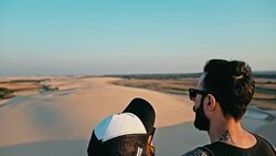 young woman and man enjoying the sunset on the peak of one of the desert sand dune Stock Footage