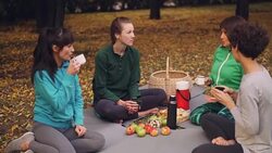 Beautiful sportswomen are relaxing after outdoor training having picnic on mats eating snacks and drinking tea. Girls are talking and laughing enjoying nature. Stock Footage