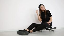 teenage girl in trendy hip hop clothes and cap posing against white wall with skateboard Stock Footage