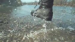 SLOW MOTION: Playful woman in furry boots running along the pure shallow river. Stock Footage