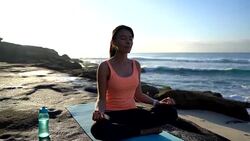 Tranquil young woman meditating next to the ocean sitting on yoga mat with eyes closed Stock Footage
