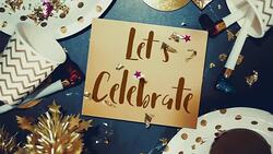 Slow motion of confetti falling down to Let’s belebrate on golden greeting card with party cup,party blower,tinsel.holiday celebration table top view Stock Footage