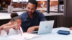 Father helps children with homework whilst mother holds baby daughter in kitchen at home - shot in slow motion Stock Footage