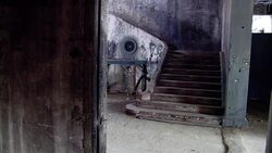 MEDIUM ANGLE OF A RUNDOWN STONE STAIRWAYS SEEN THROUGH A DOORWAY. STAIRS AND WALLS COVERED IN DIRT AND OLD PEELED PAINT. COULD BE AN ABANDONED WAREHOUSE OR MILITARY BUNKER. STAIRCASE. Stock Footage