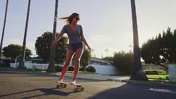 Happy care free girl skateboarding down street at sunset with hands up in air Stock Footage