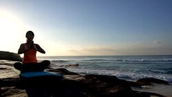 Healthy young woman practicing yoga next to the beach with eyes closed and sitting on yoga mat Stock Footage