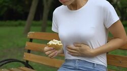 Woman eating burger in park, feeling nausea, food poisoning symptom, gastritis Stock Footage