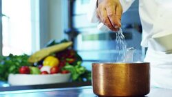 in an Italian professional kitchen a chef pours salt on a dish or in the water to boil the Italian pasta concept of healthy and light food. Stock Footage