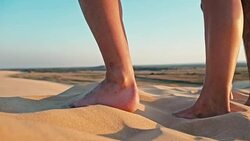 closeup of the legs of a young woman and man enjoying the sunset on the peak of one of the desert sand dune Stock Footage