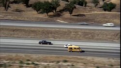 AERIAL TRACKING SHOT OF 1970'S BROWN TWO DOOR CAR DOWN FREEWAY OR HIGHWAY. SEE IT PASS OTHER CARS SUCH AS YELLOW VAN. DESERT LANDSCAPE. Stock Footage