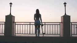 Beautiful and fashion young woman posing with a skateboard during sunrise at seafront Stock Footage
