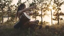 Beautiful young hippie woman with dreadlocks playing on djembe. Funky woman drumming in nature on an ethnic drum at sunset or sunrise with a human skull Stock Footage