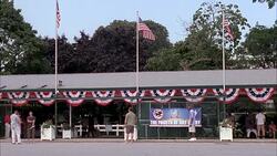 WIDE ANGLE OF ENTRANCE TO MONMOUTH PARK, HORSE RACING TRACK IN OCEANPORT, NEW JERSEY. SIGN FOR THE FOURTH OF JULY DERBY. PEOPLE, PEDESTRIANS, SPECTATORS. AMERICAN FLAGS. Stock Footage
