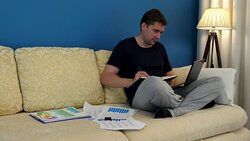 Man on a sofa with laptop is writing on a note pad. Work from home. Stock Footage