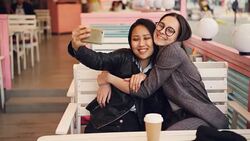 Pretty Asian girl is taking selfie with her Caucasian friend sitting at table in cafe then watching photos. Interethnic friendship, modern technology and photography concept. Stock Footage