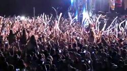 People in the stadium in front of the stage. Spotlights illuminate people in the stadium. Thousands of people in the stadium listen to music and dance. Rays of light from the stage. Many people dance under the stage. Stock Footage