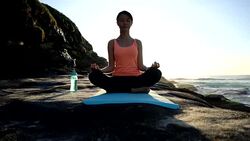 Serene beautiful woman meditating next to the sea sitting with eyes closed on her yoga mat Stock Footage