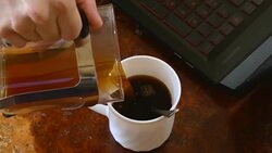 hand pouring black coffee into a white cup on wooden office desk Stock Footage