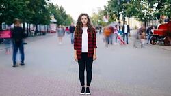 Time-lapse of attractive young woman standing in city center on busy street looking at camera wearing casual clothing while crowds of people are passing by. Stock Footage