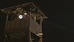 UP ANGLE OF WOODEN GUARD TOWER WITH THREE OR MORE GUARDS. SEE GUARD MOVE KLIEG LIGHT OR SEARCHLIGHT BACK AND FORTH. SEE SOLDIERS AIM AND FIRE RIFLES. SEE FLASHES OF GUNFIRE. Stock Footage