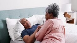 Senior woman comforting husband lying in bed at home suffering with illness - shot in slow motion Stock Footage