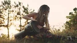 Beautiful young hippie woman with dreadlocks playing on djembe. Funky woman drumming in nature on an ethnic drum at sunset or sunrise Stock Footage