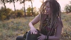 Beautiful young hippie woman with dreadlocks playing on djembe. Funky woman drumming in nature on an ethnic drum at sunset or sunrise Stock Footage