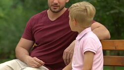 Adult man and little boy having serious conversation on bench, role model Stock Footage