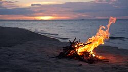 Blazing campfire on the beach during summer evening. Bonfire in nature as background. Burning wood on white sand shore at sunset. selective focus. tropical romantic landscape near sea water edge. Stock Footage