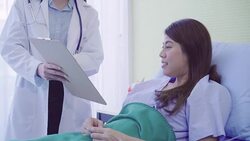 Beautiful smart Asian doctor and patient discussing and explaining something with clipboard in doctor hands while staying on Patient's bed at hospital. Medicine and health care concept. Stock Footage