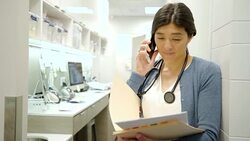 Female doctor with medical chart talking on smart phone in clinic Stock Footage