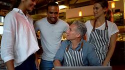 Business owner of a bakery going over some information with his team while they are all looking at laptop smiling Stock Footage
