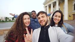 Point of view shot of multiracial group of tourists taking selfie in city center holding camera and posing together with hand gestures expressing positive emotions. Stock Footage