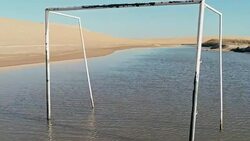 aerial footage of a beautiful blue lagoon next to the desert sand dunes with a football gate in the water Stock Footage