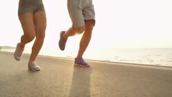 LOW ANGLE: Athletic male and female on summer vacation running along the coast. Stock Footage