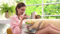 A beautiful young woman eating salad and using laptop Stock Footage