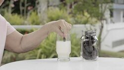 elderly hand dipping and stir a chocolate cookie In milk glass Stock Footage