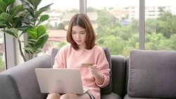Beautiful Asian woman using computer or laptop while lying on sofa in her living room. Happy female buying online shopping at home. Lifestyle woman at home concept. Stock Footage
