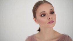 Close up slow motion portrait of beautiful woman looking at camera indoors white background text. Seductive young girl with perfect make-up pink lipstick dark eye-shadows posing in studio rack focus Stock Footage