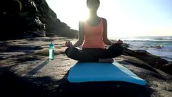 Beautiful young woman meditating next to the ocean sitting on her yoga mat with eyes closed Stock Footage