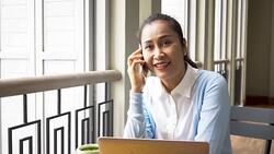 Middle age Asian woman talking on the phone while using computer and drinking green tea at coffee shop Stock Footage