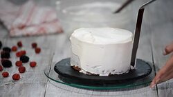 Close up of hands smearing butter cream on chocolate cake by white spatula. Stock Footage